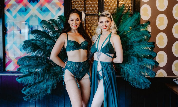 Two burlesque performers posing in teal coloured feathery costumes. 